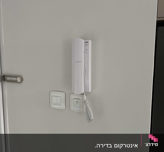 אינטרקום לבן מותקן על קיר עם כבל טלפון